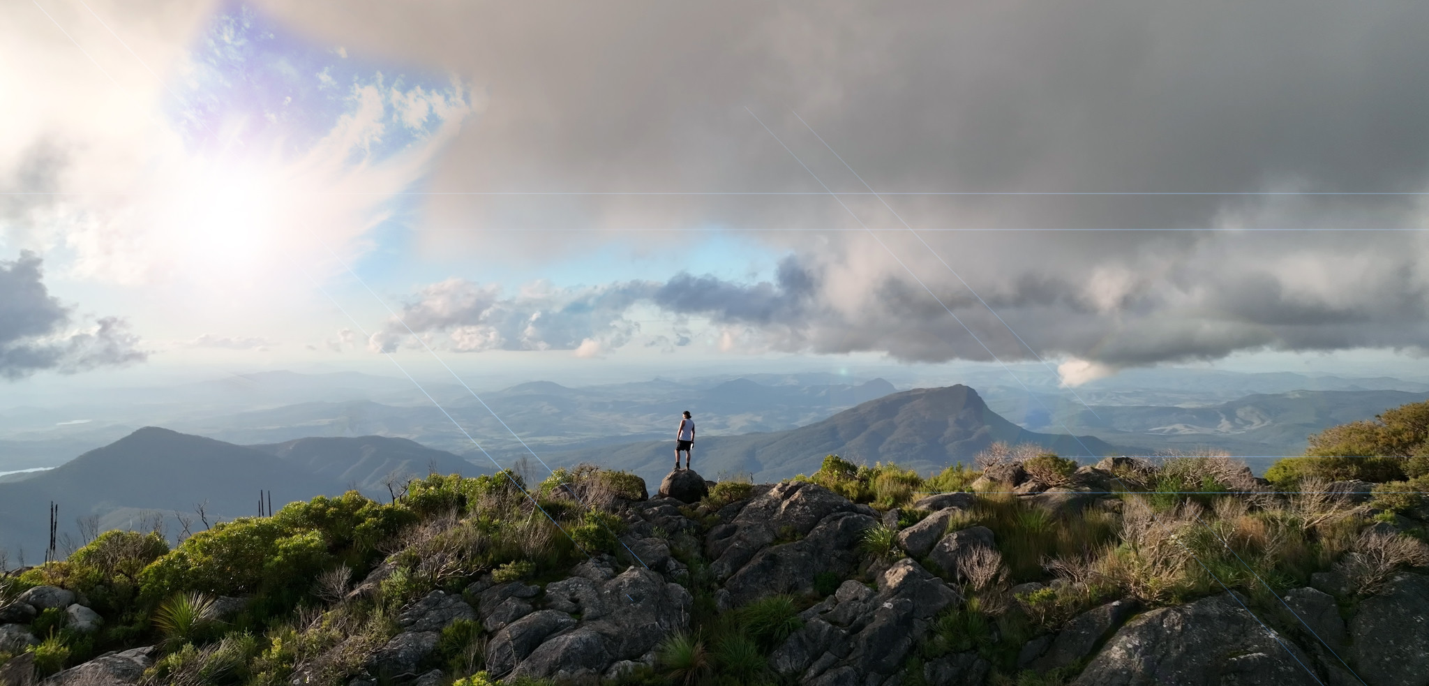 A lone figure looking across a mountain landscape from a rocky summit